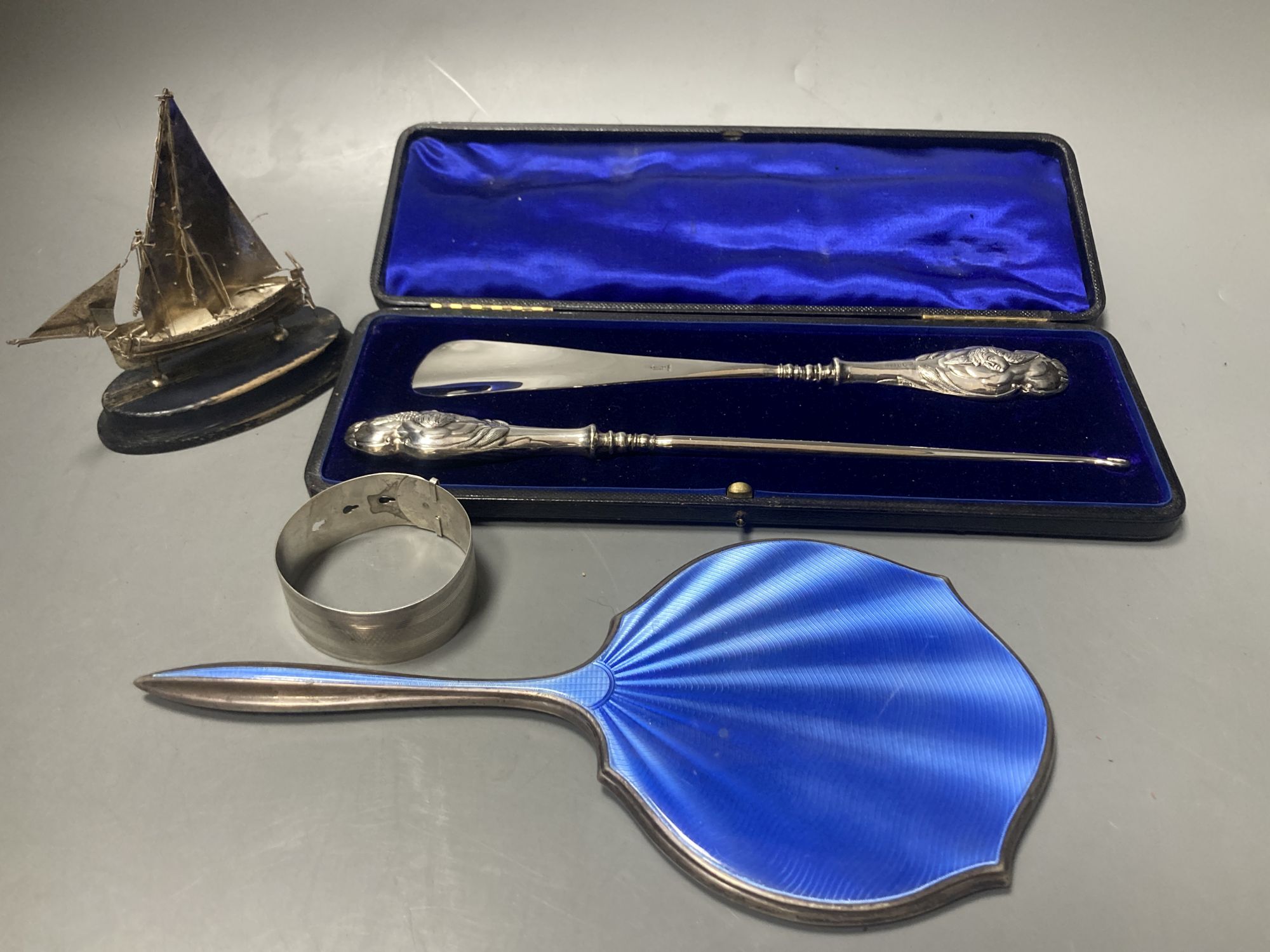 A cased silver handled button hook and shoe horn, a silver and enamel hand mirror, a silver bangle and small silver model ship
